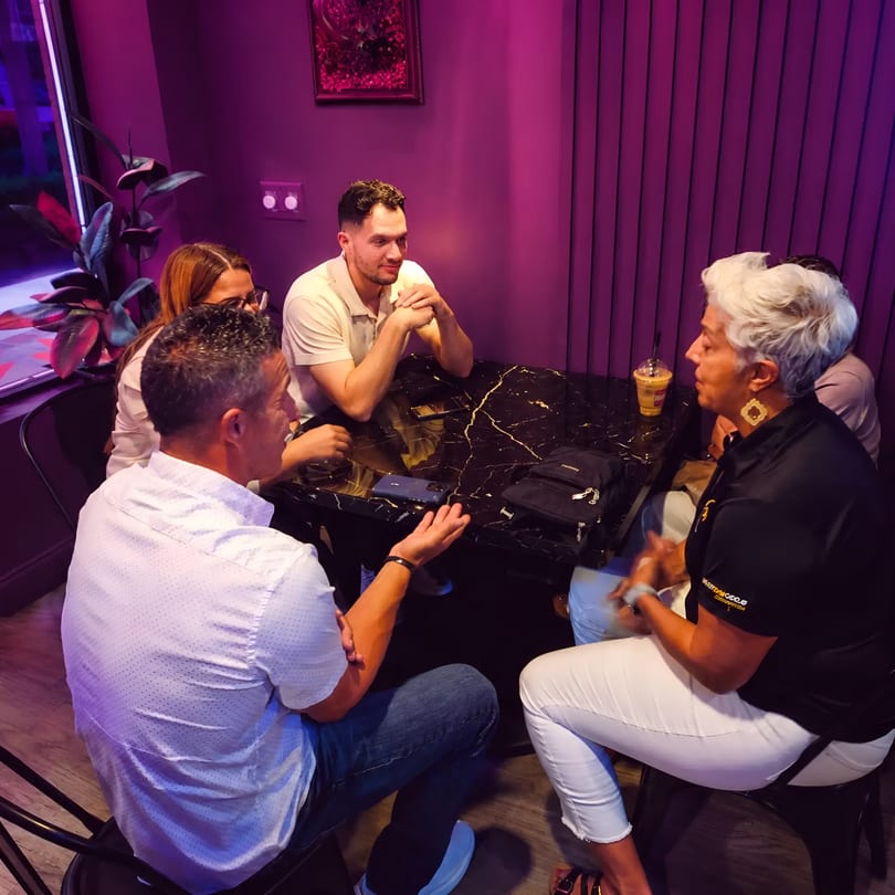 Four people conversing around a black marble table in a restaurant with purple lighting.
