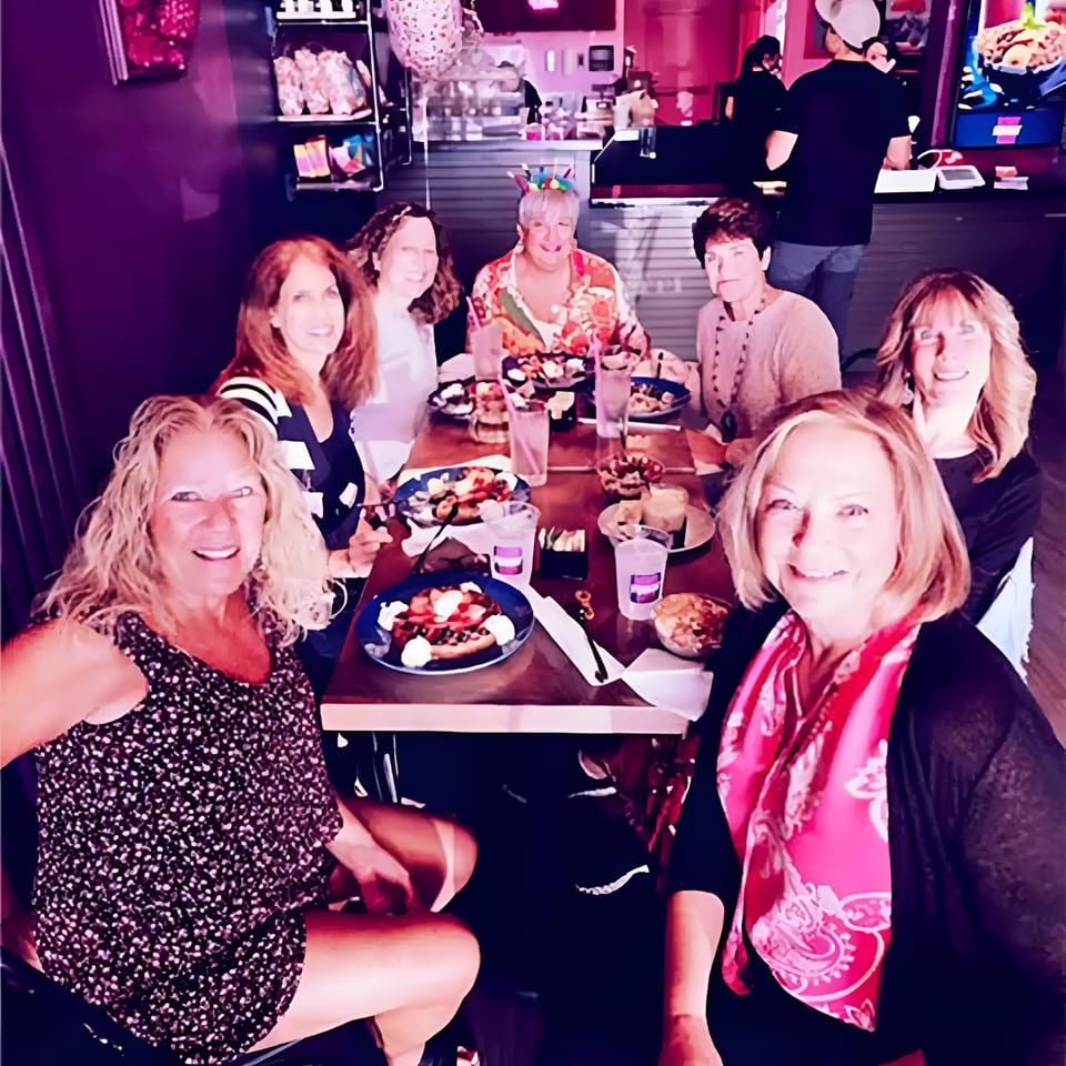 Seven smiling women enjoying a festive meal together at a restaurant table.