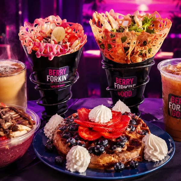 A vibrant spread of Berry Forkin' Good waffle, acai bowl, fruit cone, salad cone, and drinks.