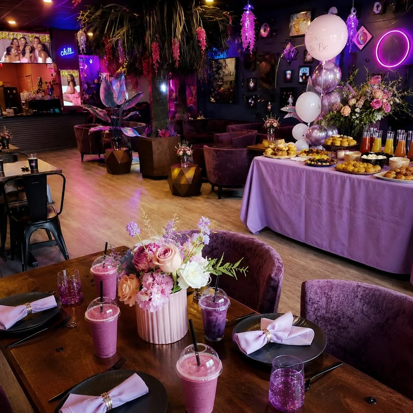Festive purple restaurant interior with buffet, set tables, lounge, and "Bride to Be" balloons.