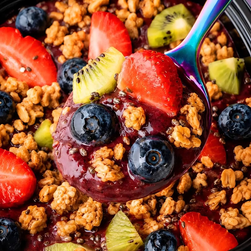 Rainbow spoon in a vibrant acai bowl topped with fresh berries, kiwi, and granola.