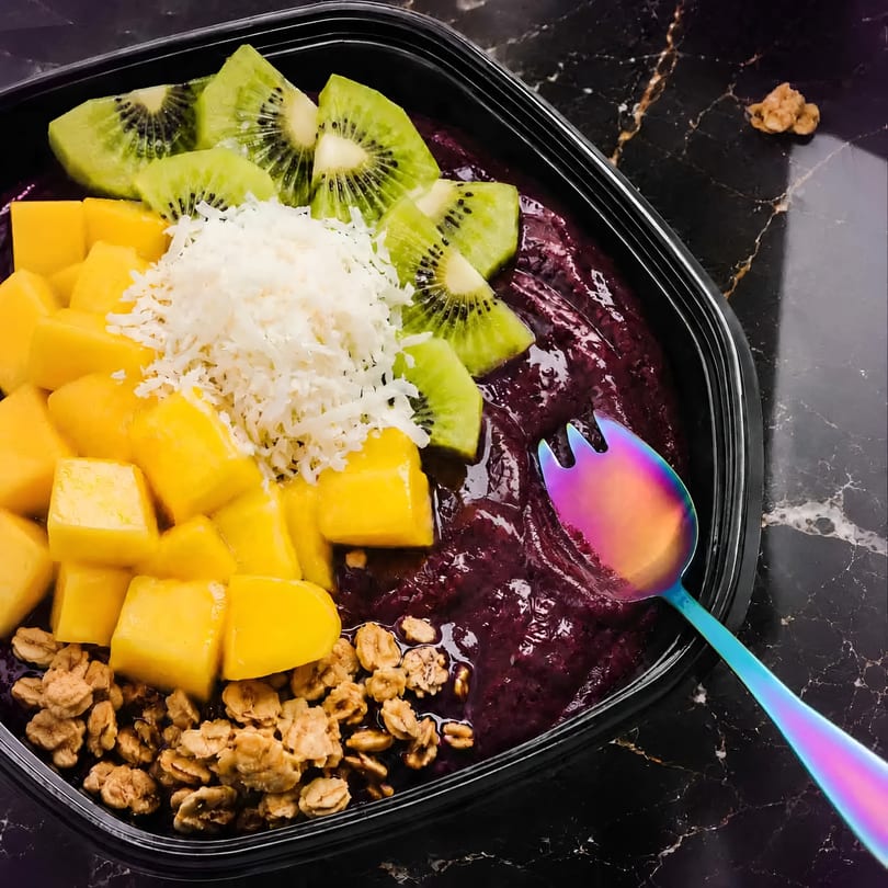 Vibrant acai bowl with kiwi, mango, coconut, granola, and a colorful spoon on marble.