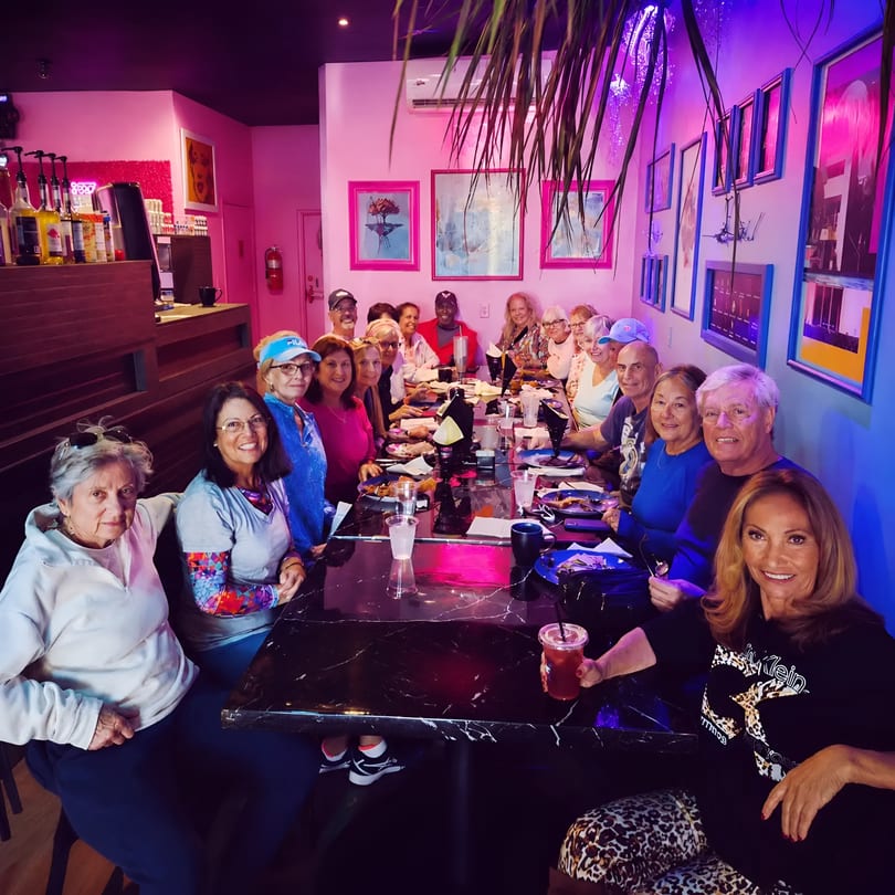 Diverse group of diners enjoying a meal at a long table in a vibrant, neon-lit restaurant.
