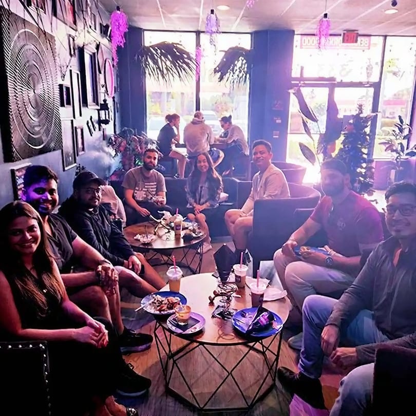 Friends gather in a vibrant, purple-lit lounge enjoying drinks and snacks.