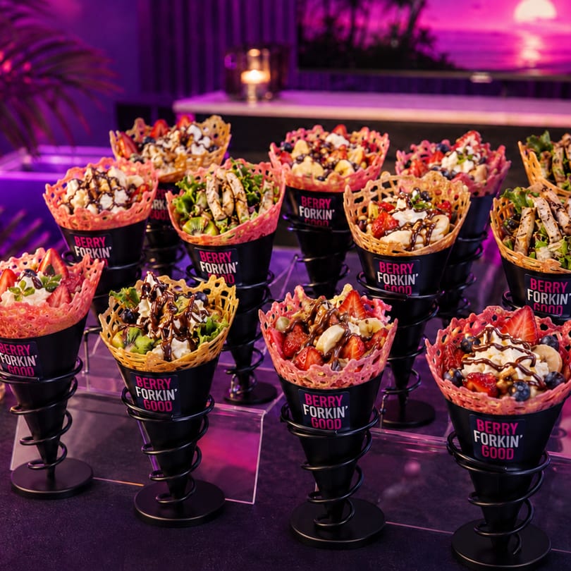 Multiple waffle cones filled with fruit, whipped cream, and chocolate drizzle, some with savory toppings.