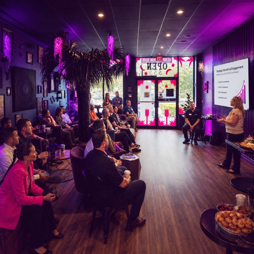 A group of people attending a presentation in a dimly lit room with purple accents.