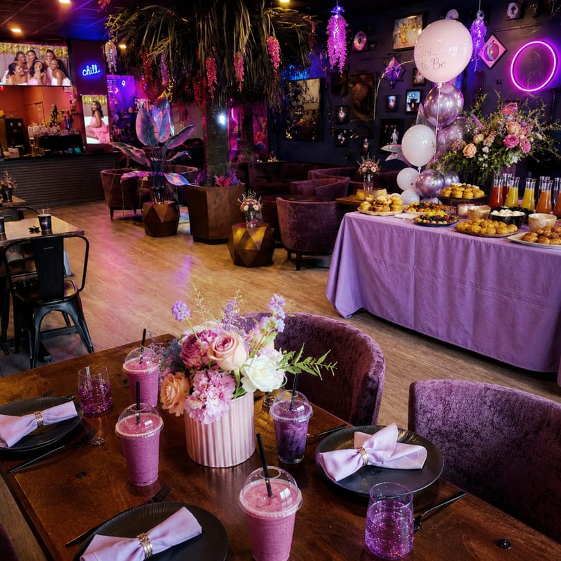 A restaurant interior decorated in purple and pink, with a buffet table and set dining tables.